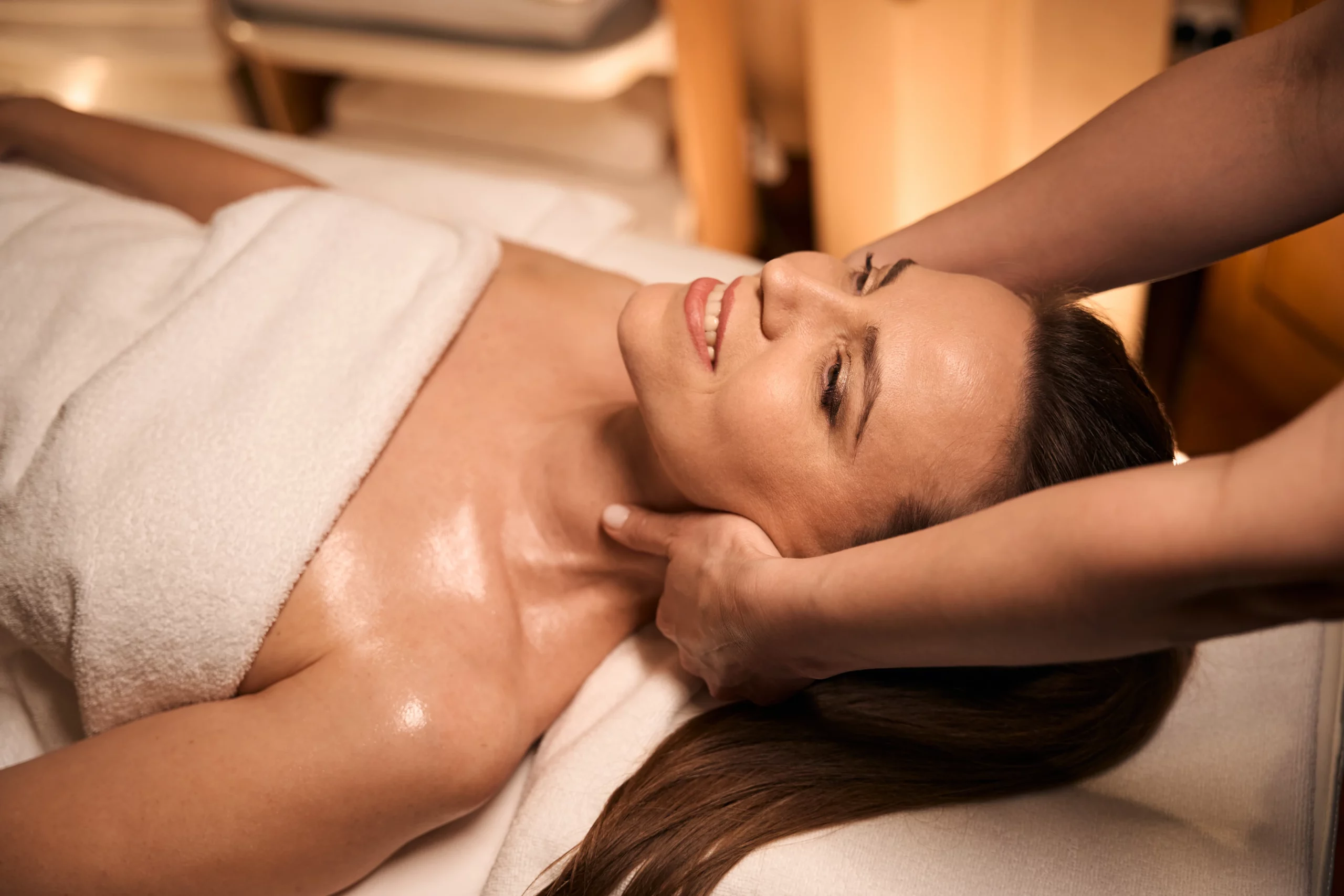Frau genießt eine entspannende Gesichtsmassage in einem Kosmetikstudio, während sie auf einer Liege mit einem Handtuch bedeckt liegt